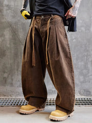 Person wearing brown wide-leg pants and yellow shoes against a gray concrete wall.