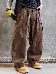 Person wearing brown baggy pants and yellow work boots against a gray concrete wall.