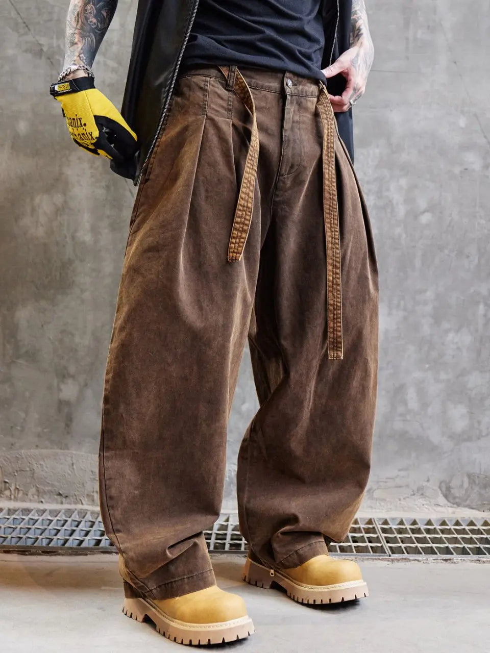 Person wearing brown baggy pants and yellow work boots against a gray concrete wall.