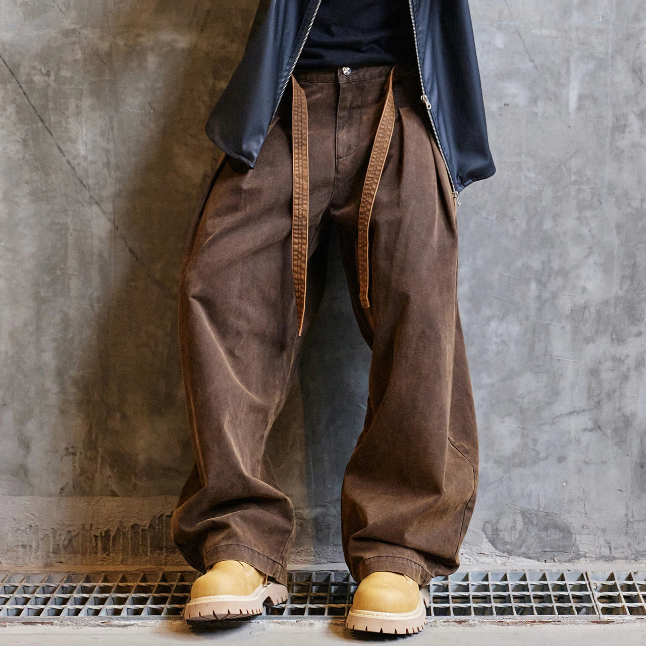 Person wearing brown wide-leg pants and yellow boots against a gray concrete wall.
