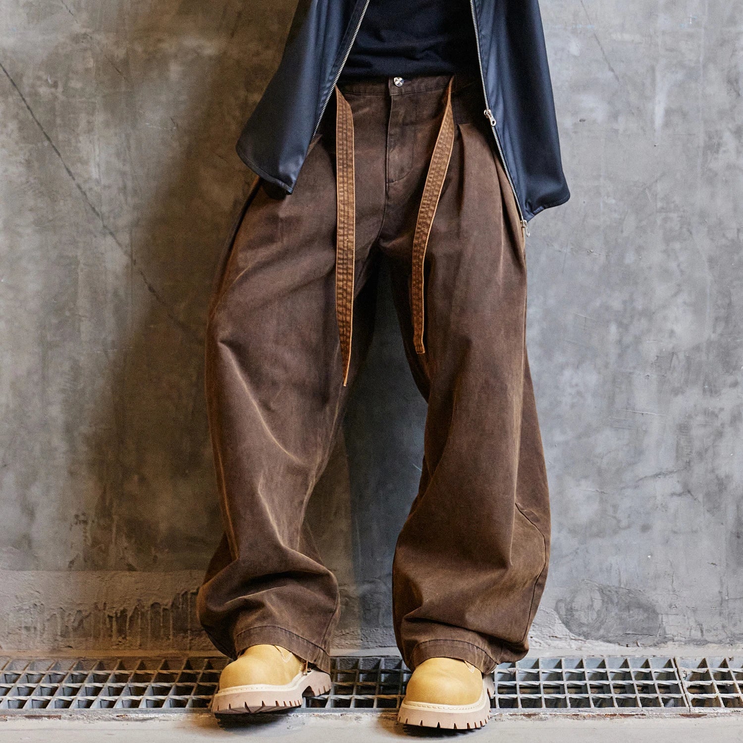Person wearing brown wide-leg pants and yellow boots against a gray concrete wall.