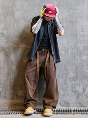 Person wearing a red cap, black jacket, brown pants, and yellow shoes against a gray concrete wall.