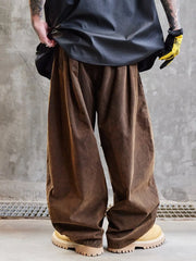 Person wearing brown wide-leg pants and a dark jacket against a gray concrete wall.