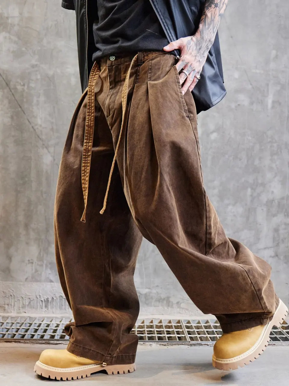 Person wearing brown wide-leg pants and yellow boots against a gray concrete wall.