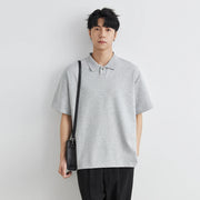 Person wearing a gray polo shirt holding a black bag against a white background