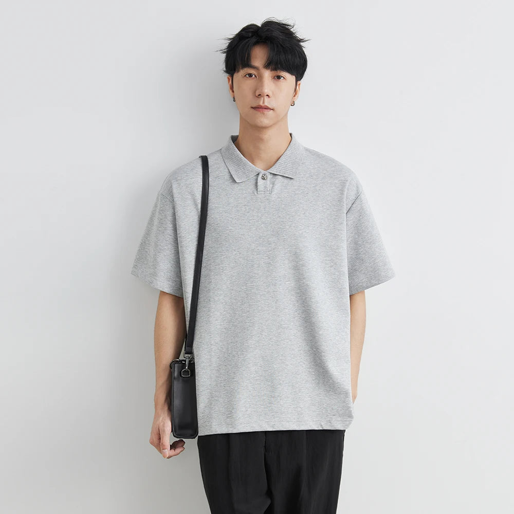 Person wearing a gray polo shirt holding a black bag against a white background