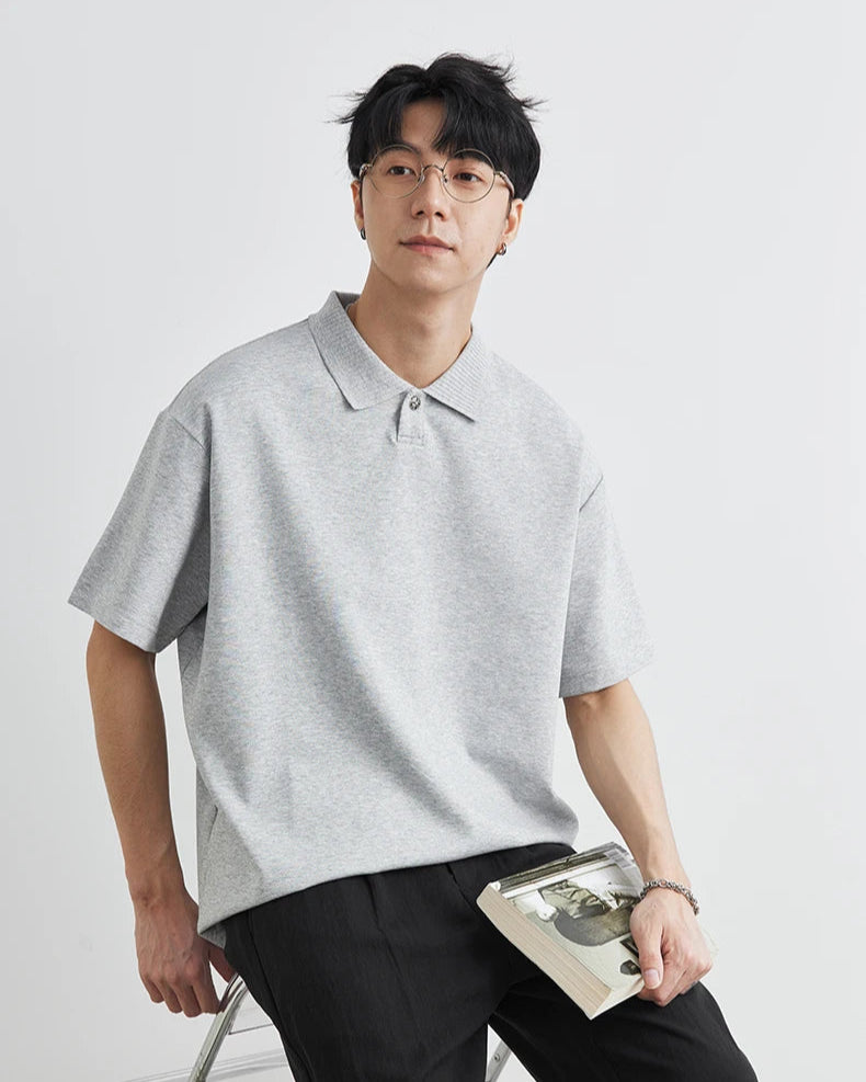 Man wearing a gray polo shirt and black pants holding a book on a white background