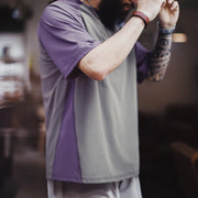 Person wearing a gray and purple shirt with tattoos on arms, blurred background