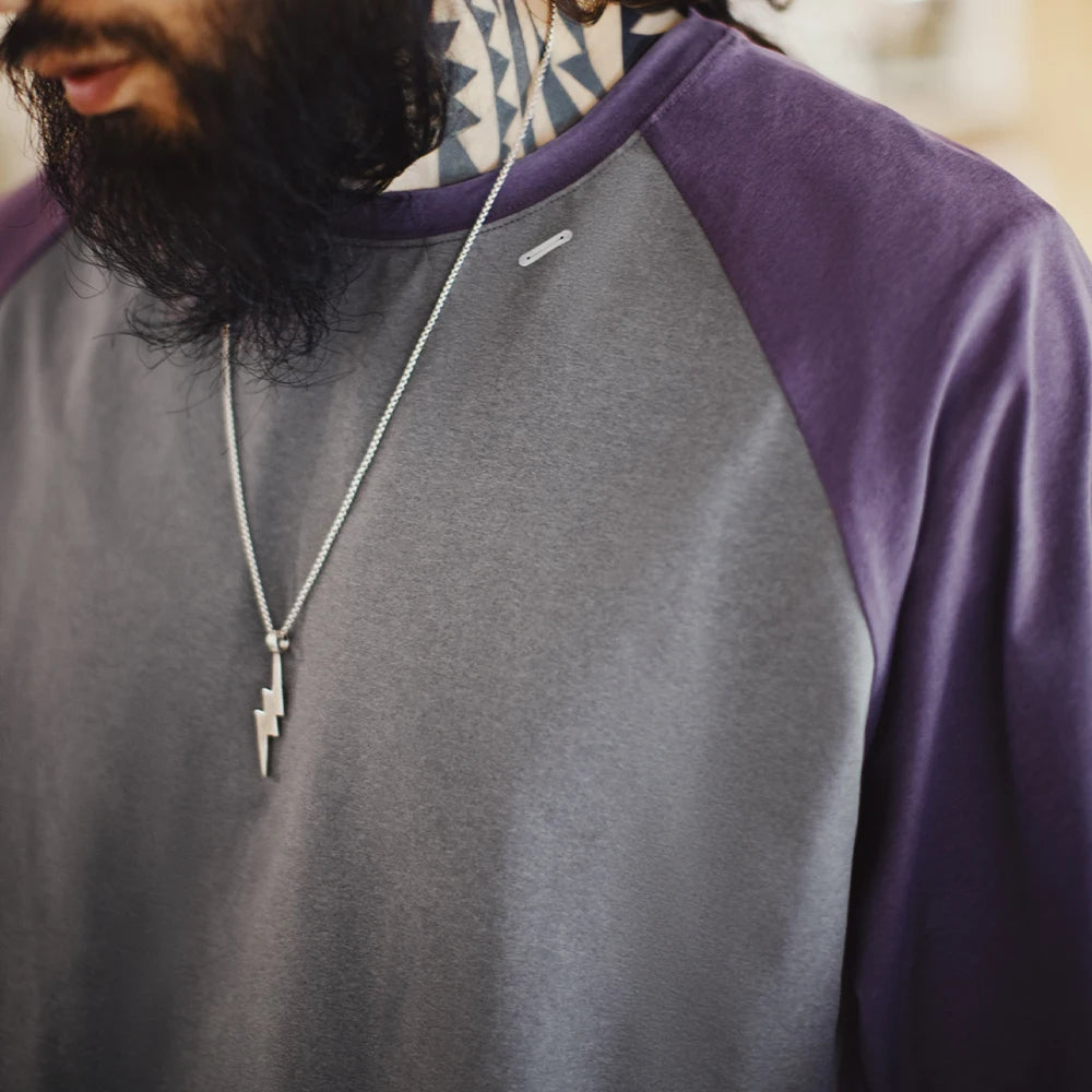 Person wearing a gray and purple long-sleeve shirt with a necklace featuring a lightning bolt pendant.