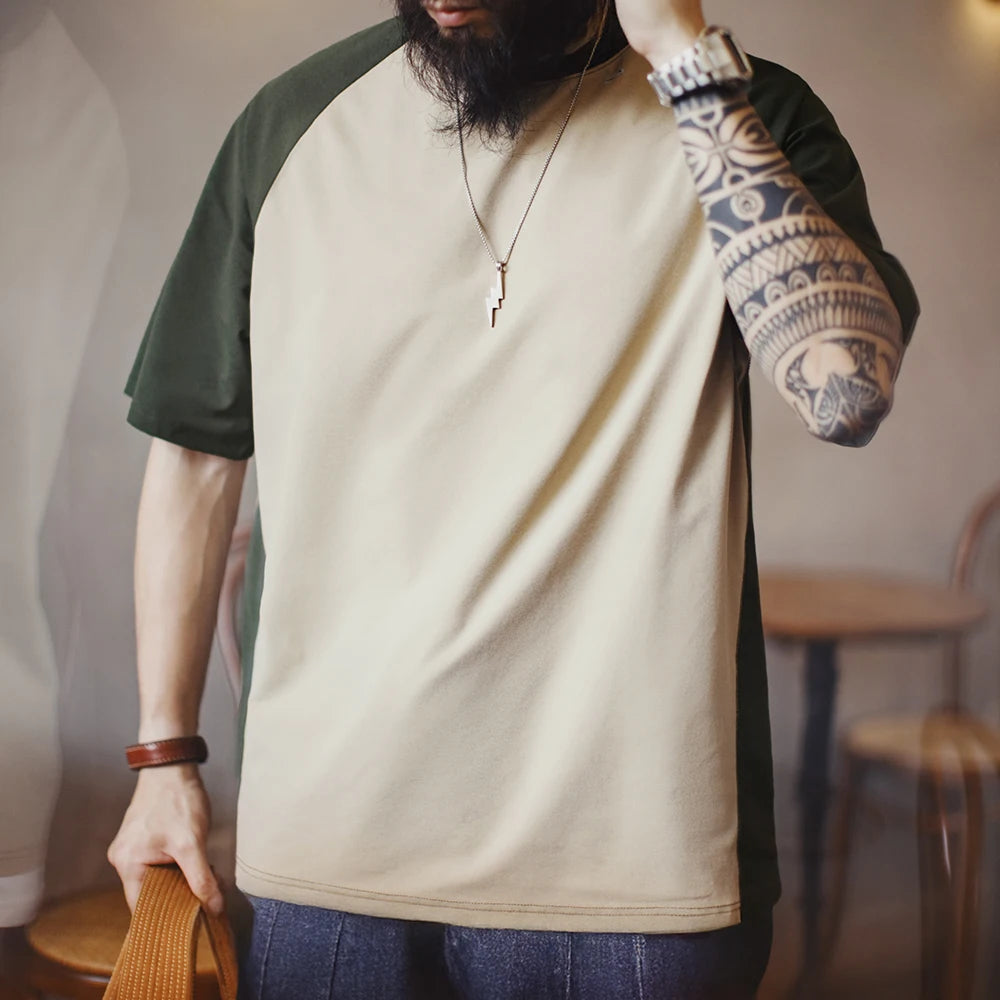 Person wearing a beige and green long-sleeve shirt with tattoos on arms, standing indoors.