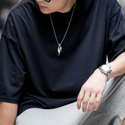 Person wearing a black shirt, silver necklace, and watch, sitting on a blurred background
