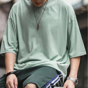 Person wearing a light green oversized shirt and dark shorts with a blurred background