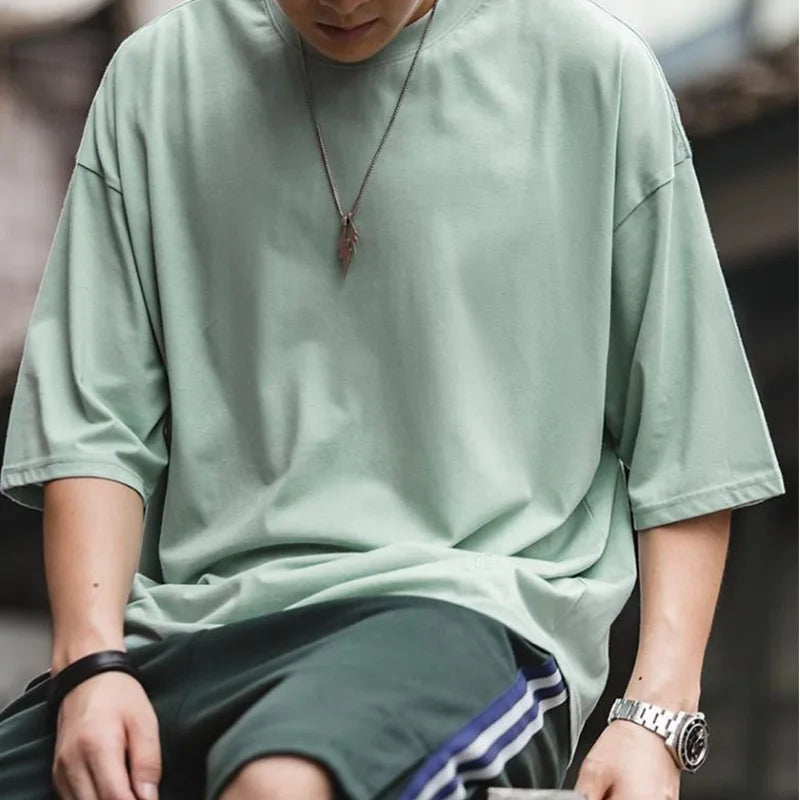 Person wearing a light green oversized shirt and dark shorts with a blurred background