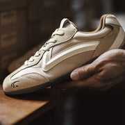 Beige sneaker with 'Speedway' branding held by a hand on a wooden surface.
