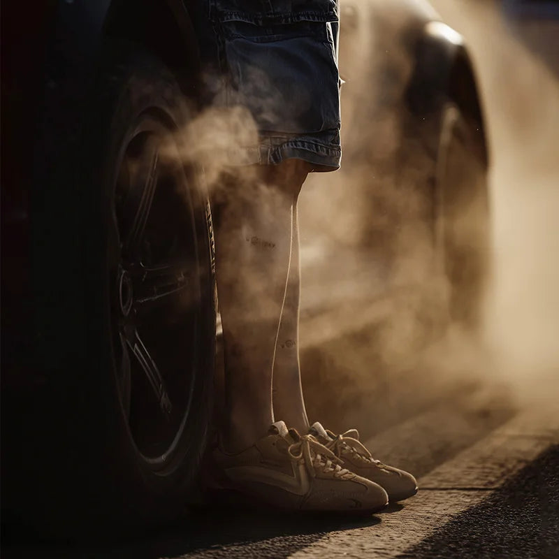 Person wearing shorts and sneakers standing next to a tire with smoke in the background