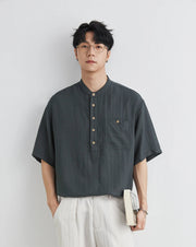 Man wearing a dark gray short-sleeve shirt with buttons against a light gray background