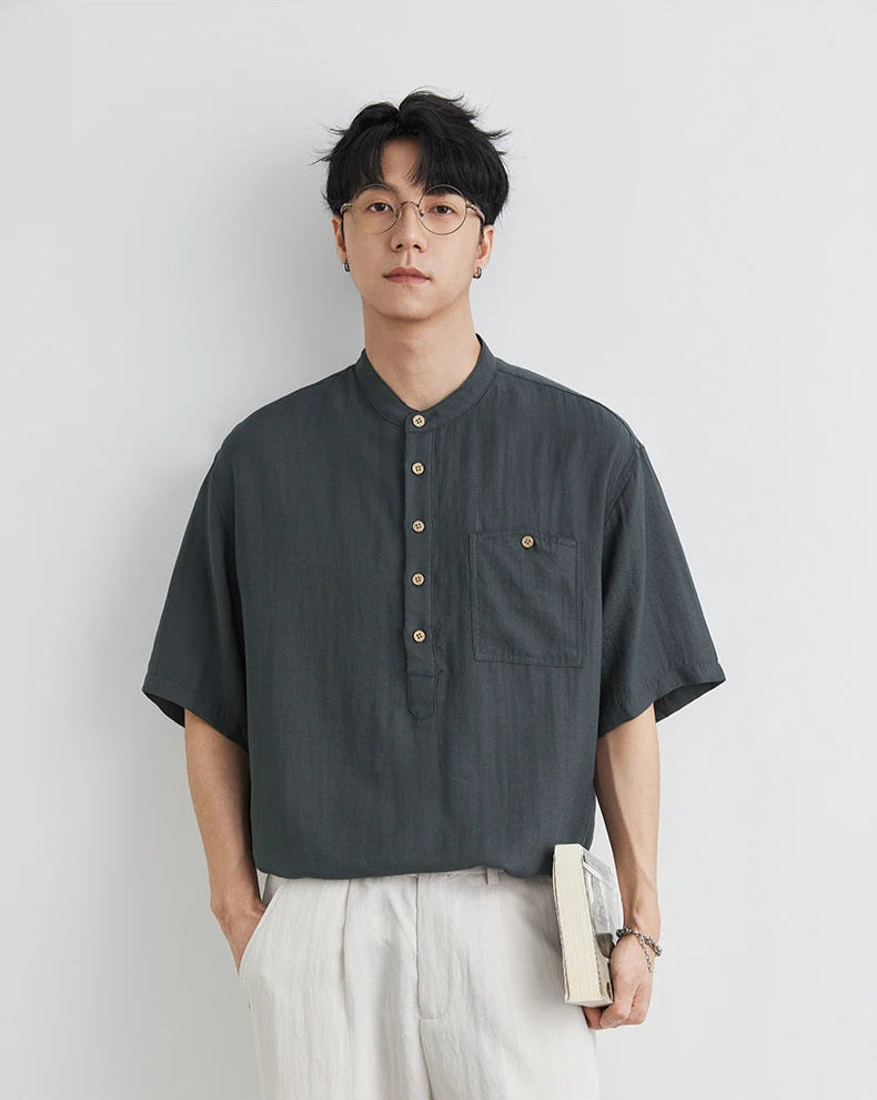 Man wearing a dark gray short-sleeve shirt with buttons against a light gray background