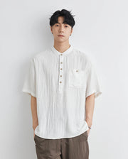 Man wearing a white short-sleeve shirt and brown pants against a light gray background