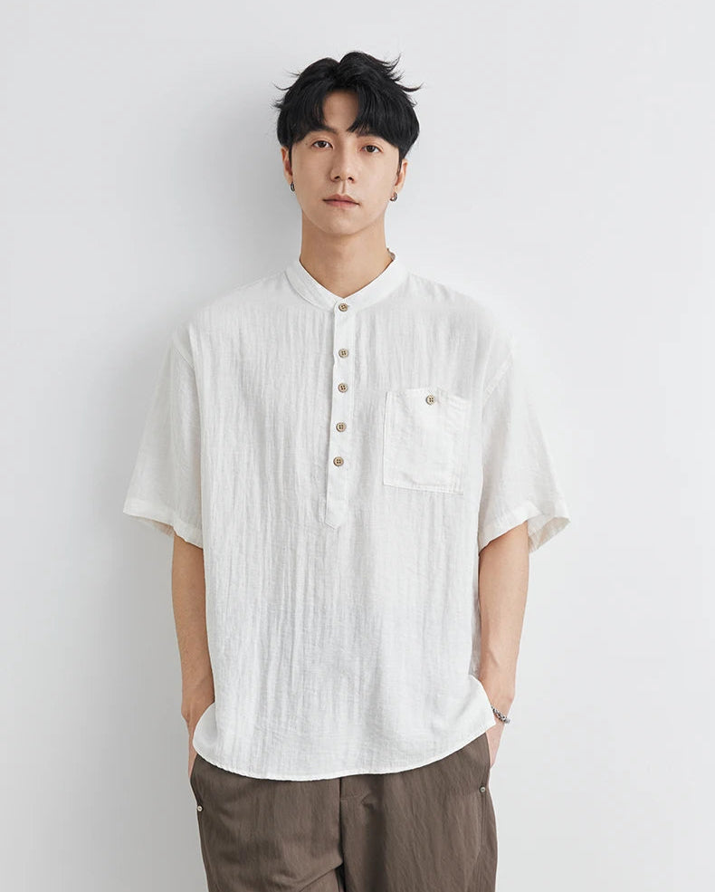 Man wearing a white short-sleeve shirt and brown pants against a light gray background