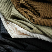 Stack of folded fabrics in various colors including green, brown, beige, and black.