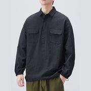 Person wearing a black textured shirt with two front pockets on a light gray background