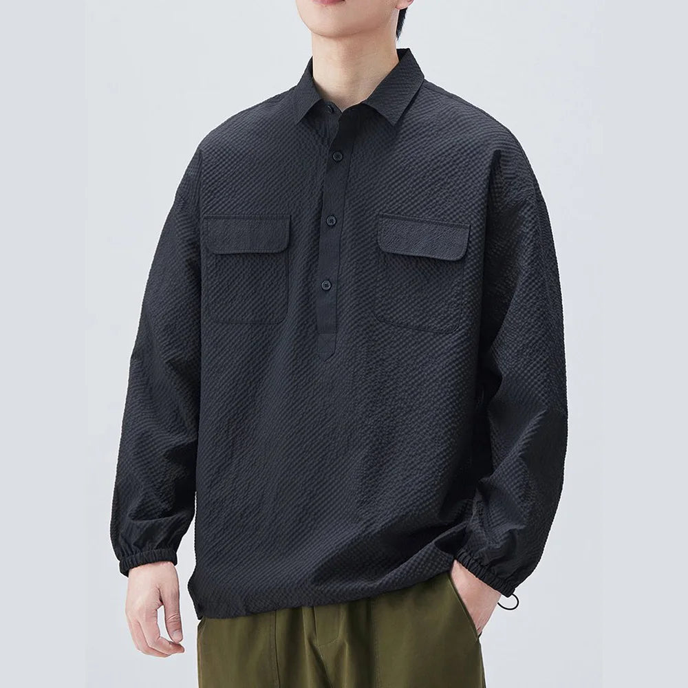 Person wearing a black textured shirt with two front pockets on a light gray background