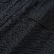 Close-up of a textured black shirt with buttons and a pocket.