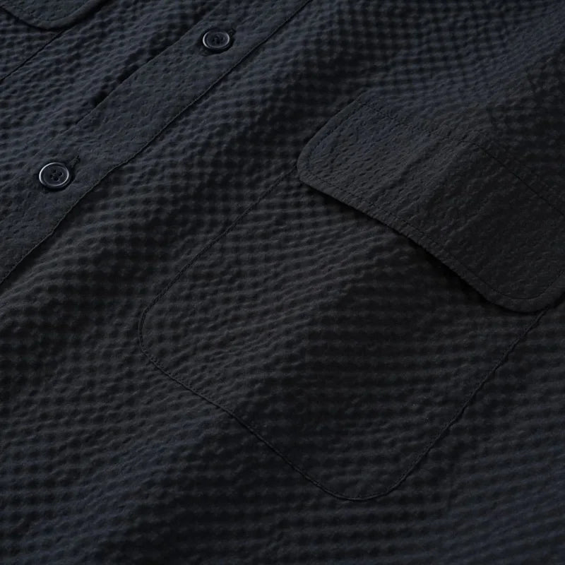 Close-up of a textured black shirt with buttons and a pocket.