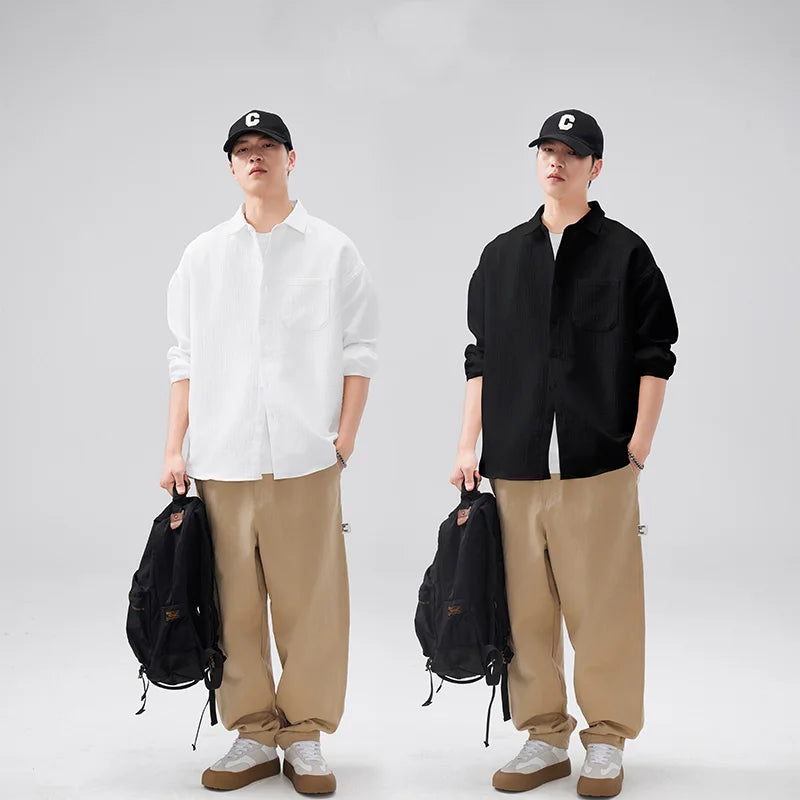 Two people wearing black caps, white shirts, and beige pants with backpacks on a plain background.