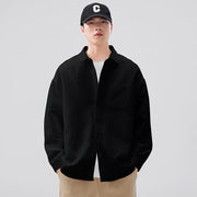 Person wearing a black jacket, white shirt, and beige pants with a black cap featuring a white logo on a light gray background.