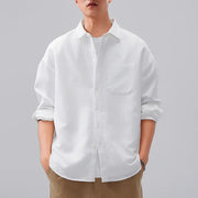 Person wearing a white button-up shirt with rolled-up sleeves on a gray background