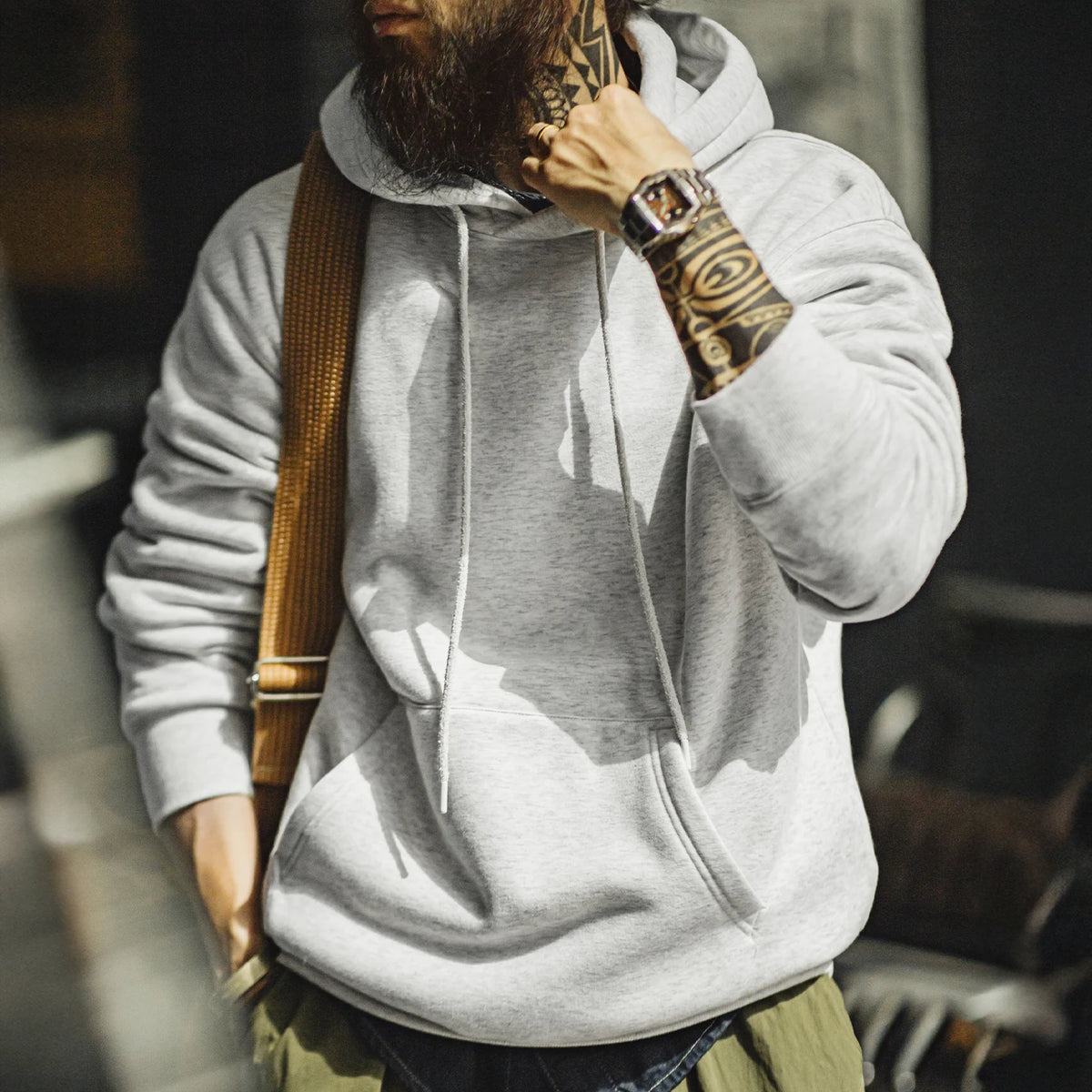 Person wearing a gray hoodie with tattoos on arms, standing outdoors.