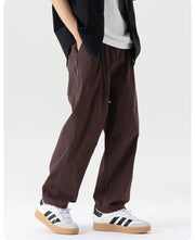 Person wearing brown pants and white sneakers with black stripes on a white background