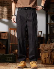 Person wearing dark gray pants and brown shoes in a casual setting with a backpack and wooden chair.