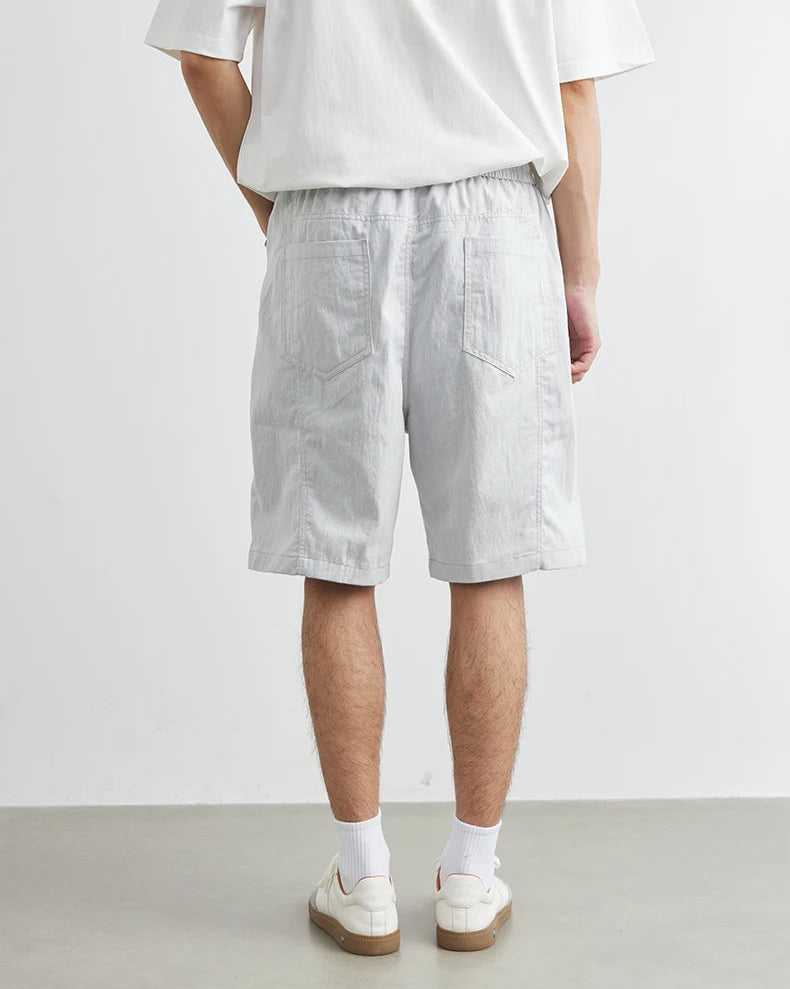 Person wearing light gray shorts and white shoes on a plain background