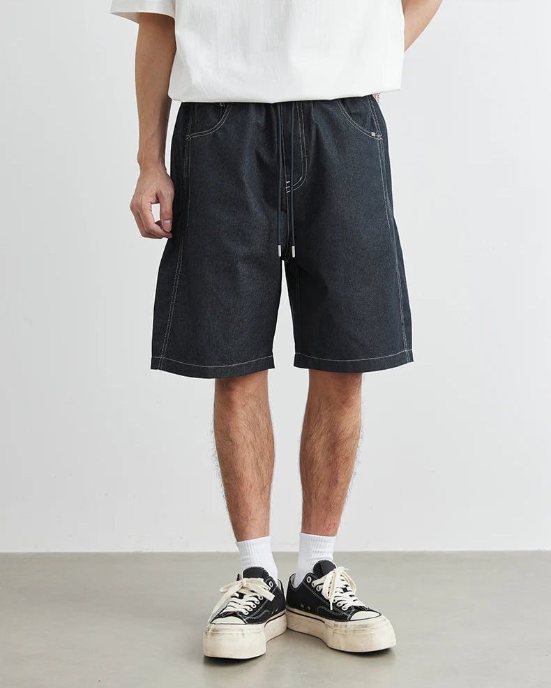 Person wearing black denim shorts and white sneakers on a plain background