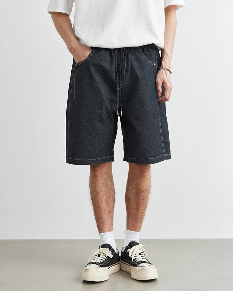 Person wearing black denim shorts and white sneakers on a plain background