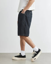 Person wearing dark denim shorts and black sneakers on a white background