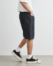 Person wearing black denim shorts and black sneakers on a white background