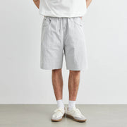 Person wearing light gray shorts and white sneakers on a plain background