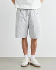 Person wearing light gray shorts and white sneakers on a plain background