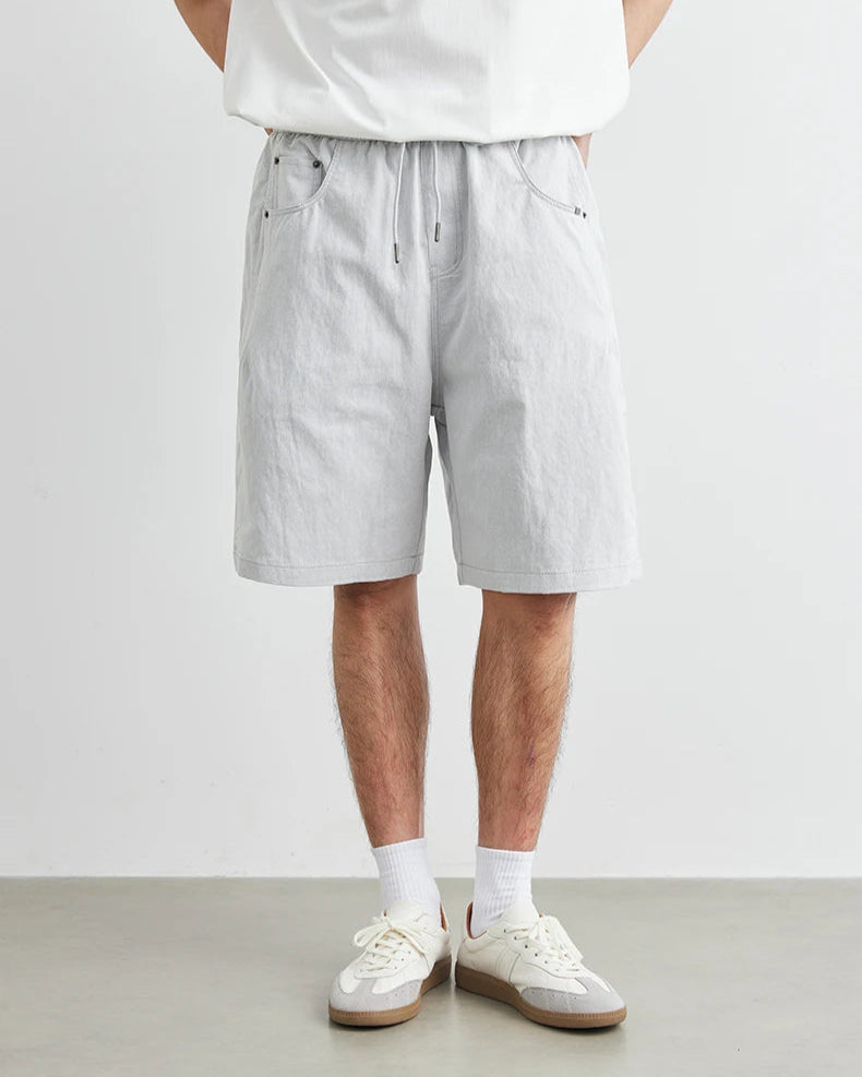 Person wearing light gray shorts and white sneakers on a plain background