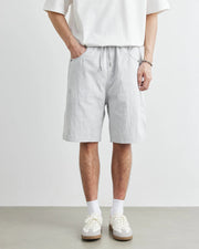 Person wearing light gray shorts and white sneakers on a plain background