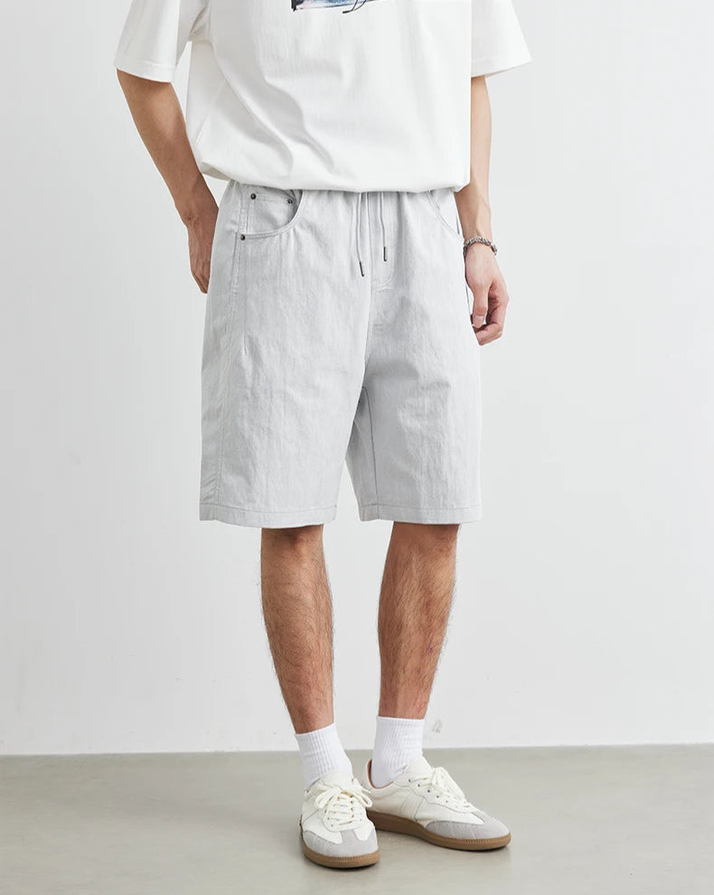 Person wearing a white t-shirt and light gray shorts on a plain background