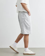 Person wearing light gray shorts and white sneakers on a plain background