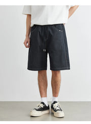 Person wearing black denim shorts and white sneakers on a plain background