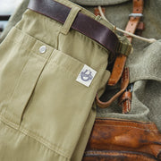 Close-up of a green military-style uniform with a leather belt and boot, featuring a brand logo on the pocket.