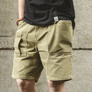 Person wearing beige shorts and a black shirt with a logo against a concrete wall.