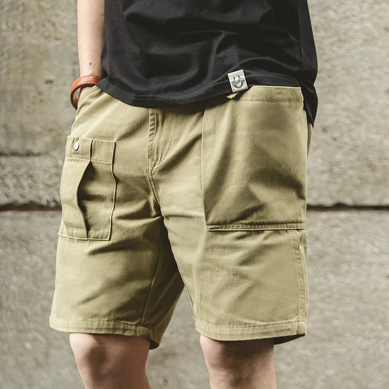 Person wearing beige shorts and a black shirt with a logo against a concrete wall.