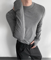 Person wearing a gray long-sleeve shirt and black pants against a white background